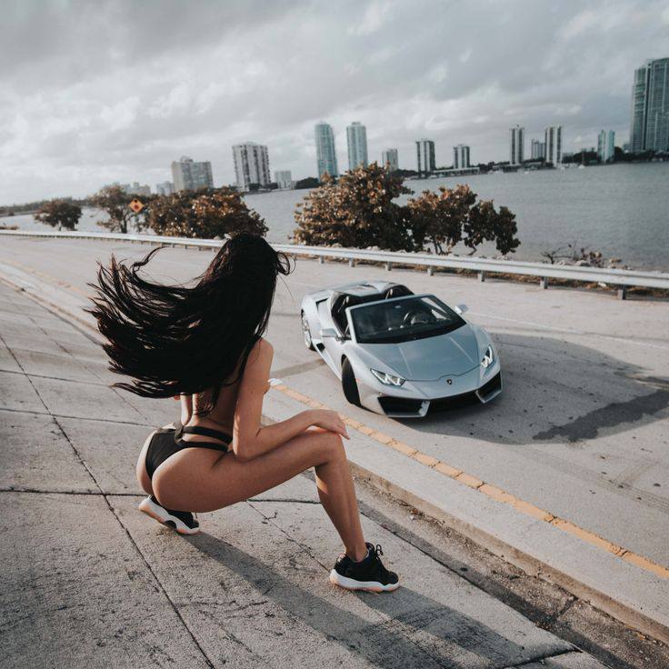 Woman in black bikini posing with white Lamborghini Huracán on Miami causeway
