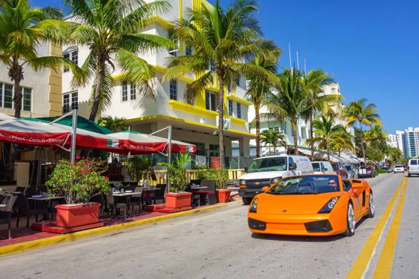 Orange Lamborghini driving on sunny Miami street with Art Deco architecture